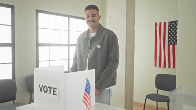Man giving thumbs up at vote booth inside a public building, wearing an i voted sticker and smiling; pride civic duty.