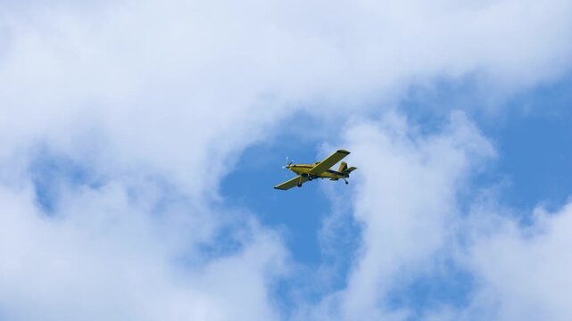 Yellow Propeller Plane Flying Through Blue Sky and Clouds
