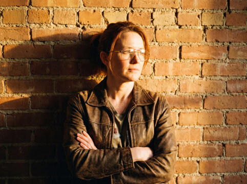 Woman with arms crossed standing against a rustic brick wall in warm sunlight