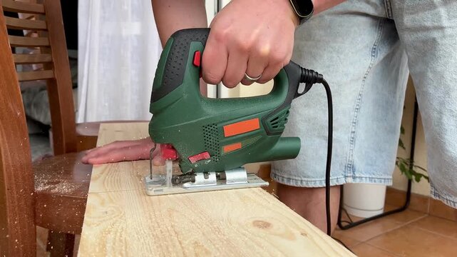 Close up of man's hands cutting pine board with jigsaw from overhead angle in slow motion 4K footage. Concept of DIY woodworking, craftsmanship and home improvement captured in cinematic detail.