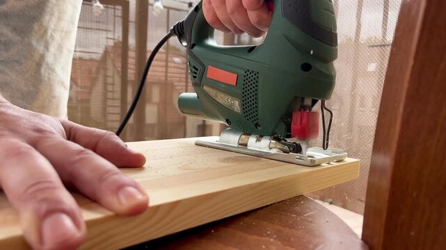 Close up of man's hands cutting pine board with jigsaw from front angle in slow motion 4K footage. Concept of DIY woodworking, craftsmanship and home improvement captured in cinematic detail.