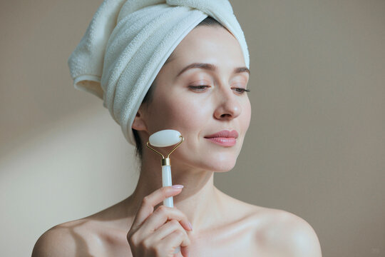 Caucasian young adult woman using facial roller during skincare routine, demonstrating self care and beauty treatment. Ideal for spa, wellness, cosmetics, anti aging marketing