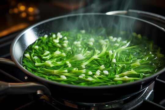 Wild garlic being blanched in a frying pan on a stove, steaming and ready for cooking