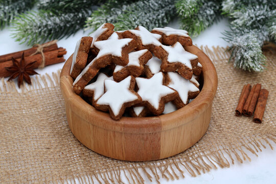 Traditional Christmas cookies&mdash;classic cinnamon stars for the Advent season, served in a wooden bowl on a jute mat with cinnamon sticks, star anise, and pine branches in a country-style arrangement.
