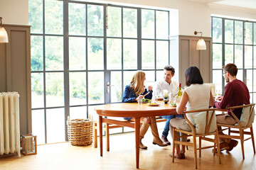 Fototapeta premium Conversation, home and couple of friends at table for lunch, dinner and social gathering with meal. Happy, house and people with food, wine and talking for bonding, connection and reunion for visit