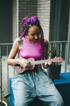 A tattooed woman with purple braids playing ukulele