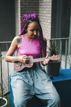 Woman with purple braids playing ukulele on balcony
