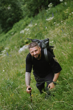 Tattooed man winks while hiking up a green hill