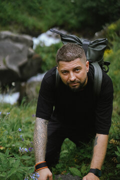 Tattooed man with a backpack climbing a hill