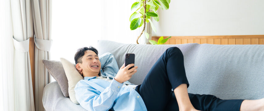 ソファに寝転んでスマートフォンを使う男性