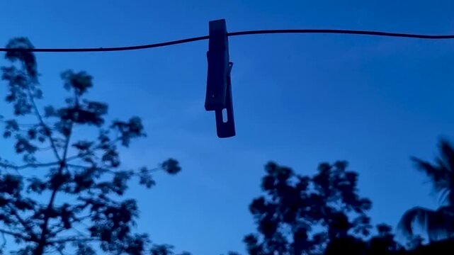 Single clothespin hanging on a line against a deep blue evening sky peg clothesline wire dusk