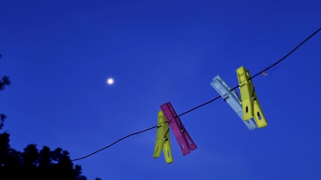 Colorful clothespins attached to a wire against a night sky with moon clothespin peg clothesline