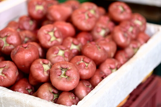 Reddish-pink wax apples with uneven natural coloring and worn skin fill a white styrofoam box, a red plastic crate blurred behind, Huaxin Street, Zhonghe.