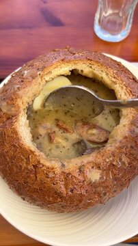 Traditional Polish zurek soup served in a bread bowl is stirred with a spoon, showcasing a classic Polish dish