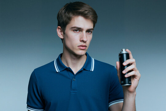 Portrait of Caucasian young adult man holding aerosol spray can, presenting personal care or grooming product against plain background. Useful for mens cosmetics advertising and packaging