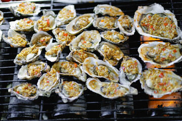 Oysters grilling with garlic chili sauce on charcoal grill night market Sanya, Hainan Island, China © Parilov