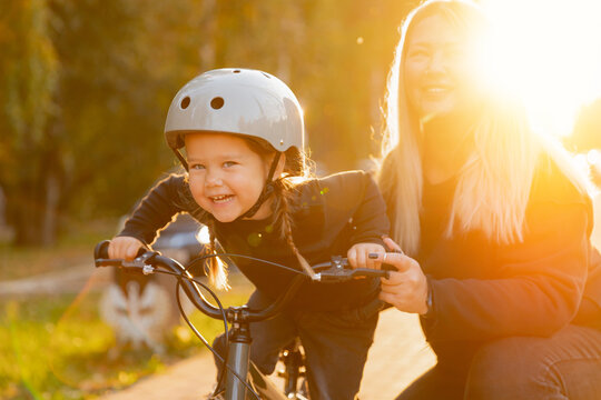 Caucasian mother guides young daughter learning to ride bicycle in sunlit park
