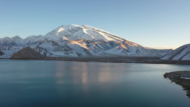 Aerial view of sunrise over Muztagh Ata and Karakul Lake in Xinjiang, China, showing golden snow mountain reflection