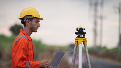 Civil engineers and survey team using a total station theodolite and road construction plans to...
