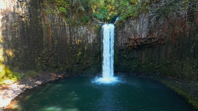 Waterfall plunging into a tranquil pool at Abiqua Falls, Oregon beneath basalt cliffs, drone orbit right