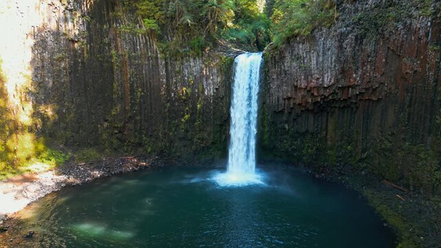 Waterfall and emerald pool at Abiqua Falls, Oregon surrounded by rugged basalt walls, drone angled orbit left