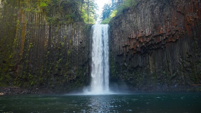 Waterfall plunging into a clear pool at Abiqua Falls, Oregon beneath basalt cliffs in soft light, geometric hexagonal pillars, low establishing
