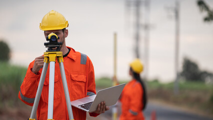 Civil engineers and survey team using a total station theodolite and road construction plans to...