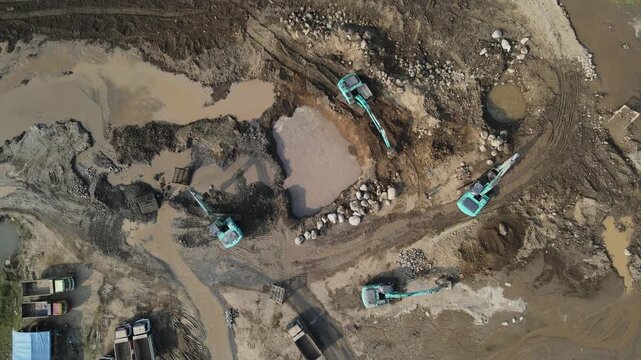Aerial Footage of Large-Scale Rock and Sand Quarry with Excavator and Mining Truck Covered in Mud, Surrounded by Cloudy Water and Distinctive Soil Textures. 