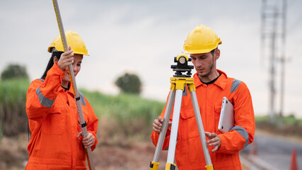 Civil engineers and survey team using a total station theodolite and road construction plans to...