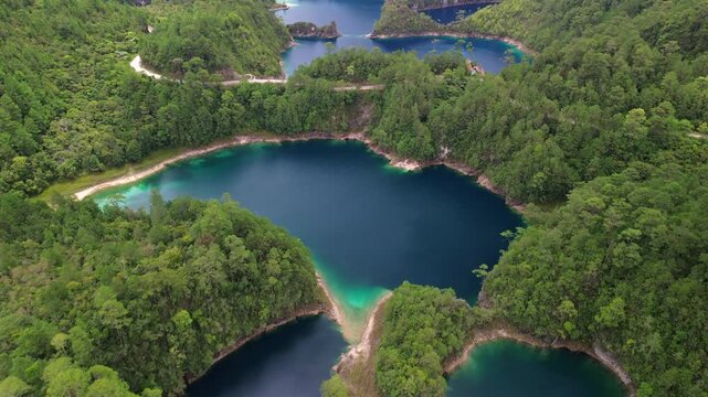Slow aerial drone forward shot revealing a deep blue crater lake with turquoise shoreline surrounded by pine forest in Montebello, Chiapas, Mexico.