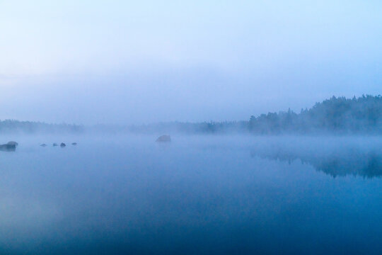 Dichter Nebel &uuml;ber einem stillen See w&auml;hrend der blauen Stunde fr&uuml;h morgens