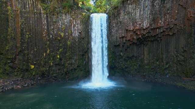 Waterfall dropping into a calm pool at Abiqua Falls, Oregon beneath basalt cliffs, drone medium static