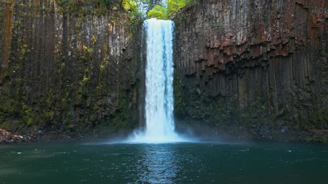 Centered waterfall above emerald pool at Abiqua Falls, Oregon enclosed by basalt canyon, drone low pullback
