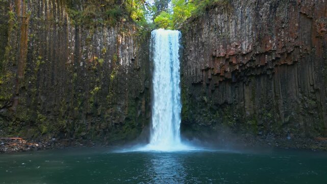 Waterfall descending into a clear pool at Abiqua Falls, Oregon framed by basalt cliffs, drone low medium approach