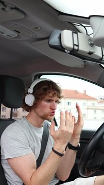 Vertical screen driver dances in headphones while the car remains stationary illustrating how loud music can reduce road awareness and become a distraction during driving
