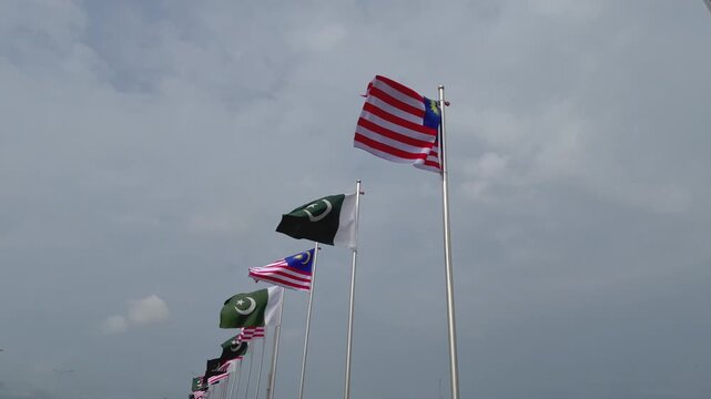 Pakistan and Malaysia Flags Waving Together Against a Dramatic Cloudy Sky, International Relations Concept