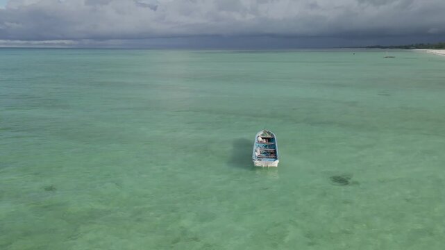 A video focussing on a traditional boat in the sea off the coast of Paje, Zanzibar, Tanzania. The drone pivots around the boat whilst keeping it in the middle of the shot and reveals the beach