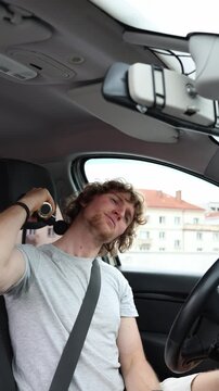 Vertical screen tired driver uses an electric massage gun to relax his fatigued neck muscles in the parked sedan after stiffness developed during a long demanding journey
