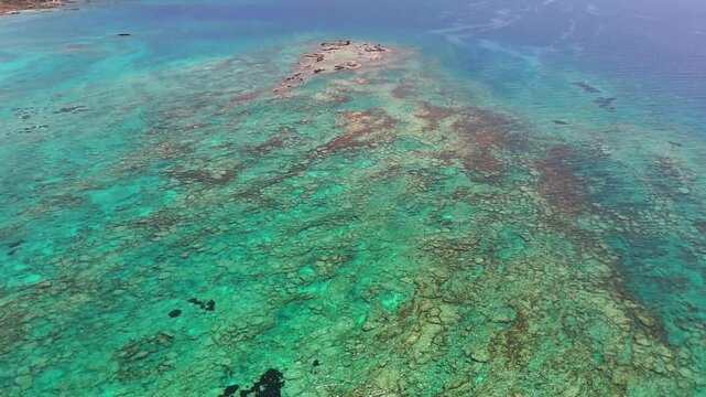 Elafonissi lagoon reveals turquoise shallows, exposed limestone formations and textured seabed along southwestern Crete, Greece, drone forward flyover.