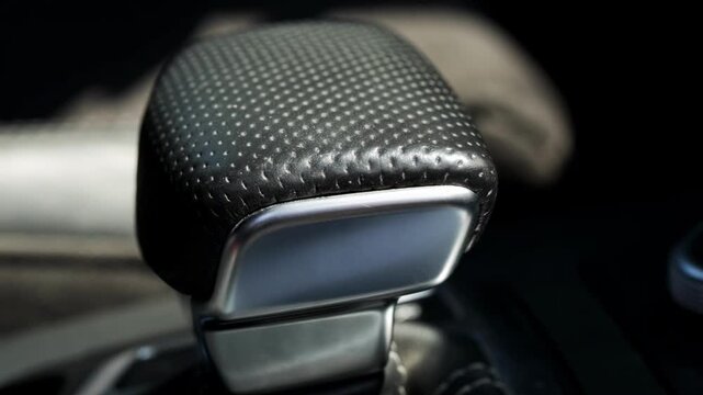 Close-up view of modern luxury car automatic gear selector lever, featuring textured perforated black leather finish and polished silver metal accents, DSG