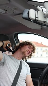 Vertical screen driver massages his sore neck with an electric massage gun inside the parked vehicle easing muscle tension and stiffness after one long exhausting journey