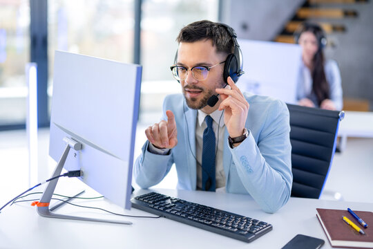 Male customer support agent pointing at computer screen in office