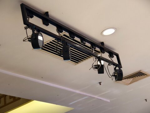 Modern black track lighting fixture with adjustable LED spotlights installed on a commercial ceiling near central air conditioner vents.