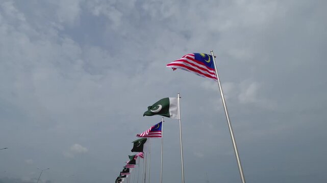 Pakistan and Malaysia Flags Waving Together Against a Dramatic Cloudy Sky, International Relations Concept