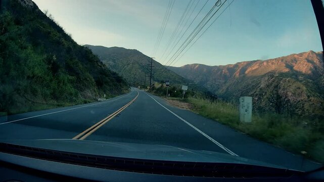 A dashcam view of Malibu Canyon Road. Mountain road driving experience during sunrise or sunset, showcasing winding asphalt highway through rugged canyon landscape.