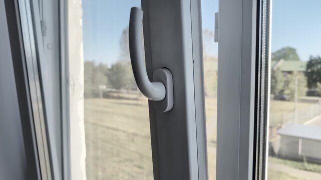 Male hand turning PVC window door handle for ventilation purpose at home. Close view of one person closing plastic frame window mechanism indoors during daytime
