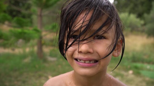 A close-up shows a wet boy with disheveled hair smiling outdoors after swimming, Close-Up Portrait Shot