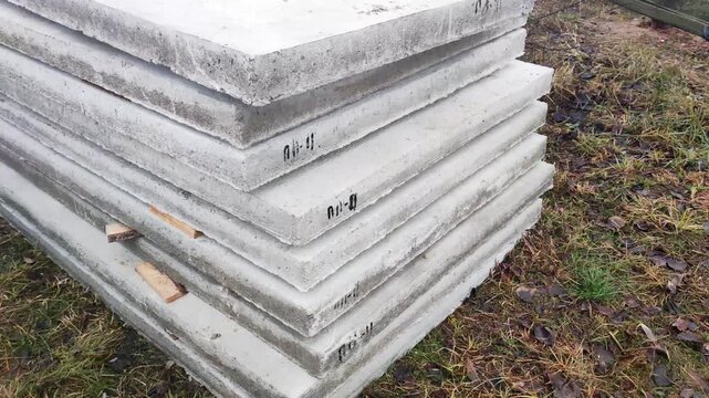 Stacked concrete slabs ready for construction project outdoors, gray building materials neatly piled on dry ground awaiting use, industrial supplies for foundation or pathway work