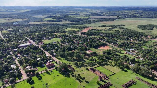 Aerial landscape view of ancient Jesuit mission ruins surrounded by lush trees and rural paths in Paraguay.
