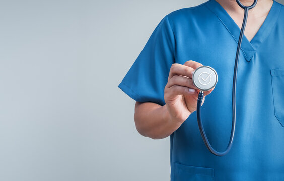 Healthcare professional in blue scrubs presents stethoscope with check mark with copy space. Preventive screening, medical checkups, patient safety, trusted care, and healthcare quality concept.